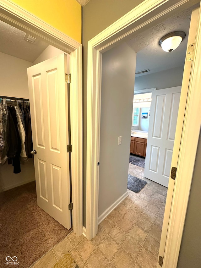 hall featuring baseboards, a textured ceiling, and light colored carpet