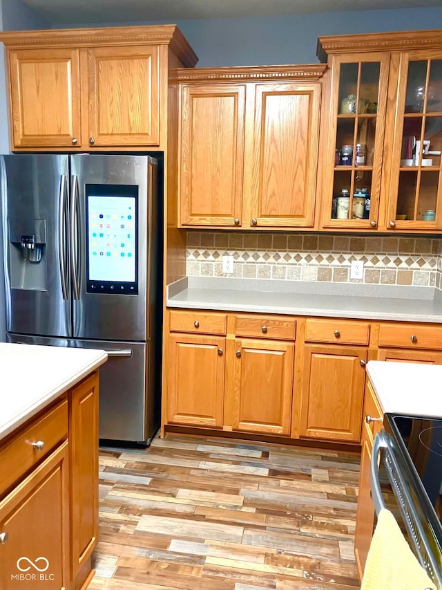 kitchen with stainless steel fridge, light countertops, light wood-type flooring, decorative backsplash, and glass insert cabinets
