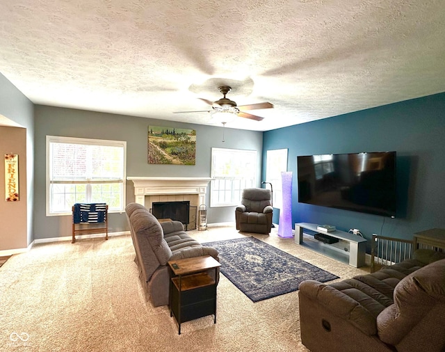 carpeted living room featuring ceiling fan, plenty of natural light, a textured ceiling, baseboards, and a tile fireplace