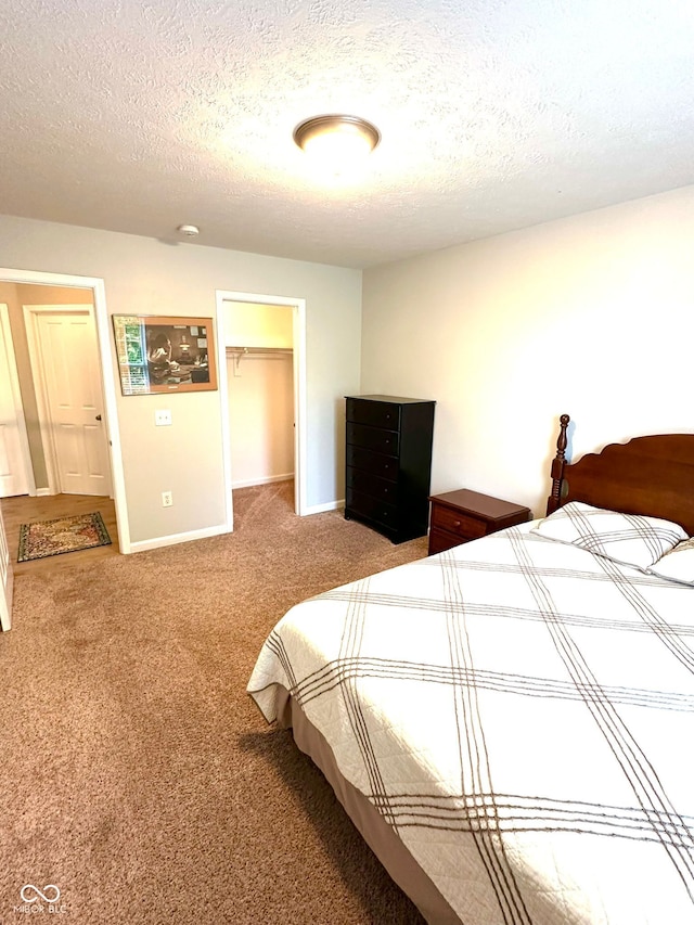 carpeted bedroom with a textured ceiling, baseboards, and a spacious closet