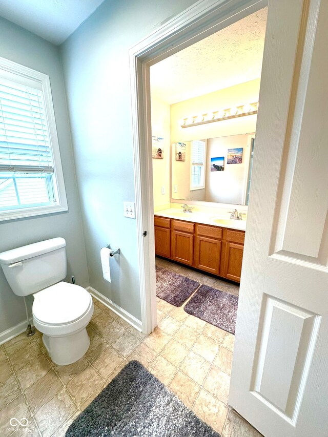 bathroom featuring toilet, baseboards, and double vanity