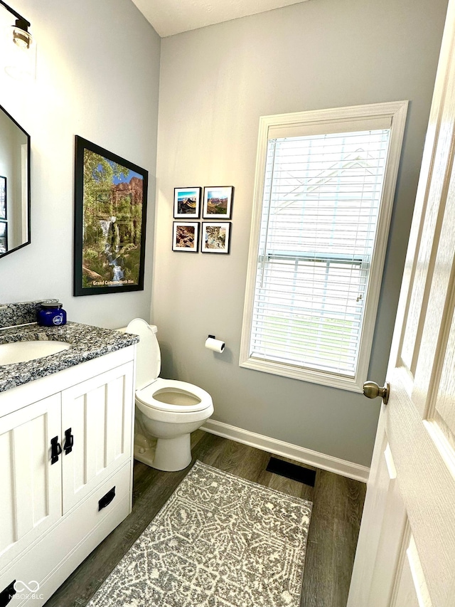 bathroom with wood finished floors, toilet, plenty of natural light, and vanity