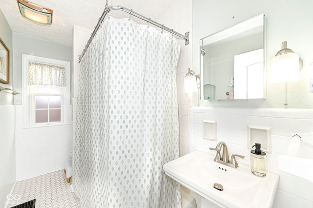 full bathroom featuring visible vents, curtained shower, tile walls, a textured ceiling, and a sink