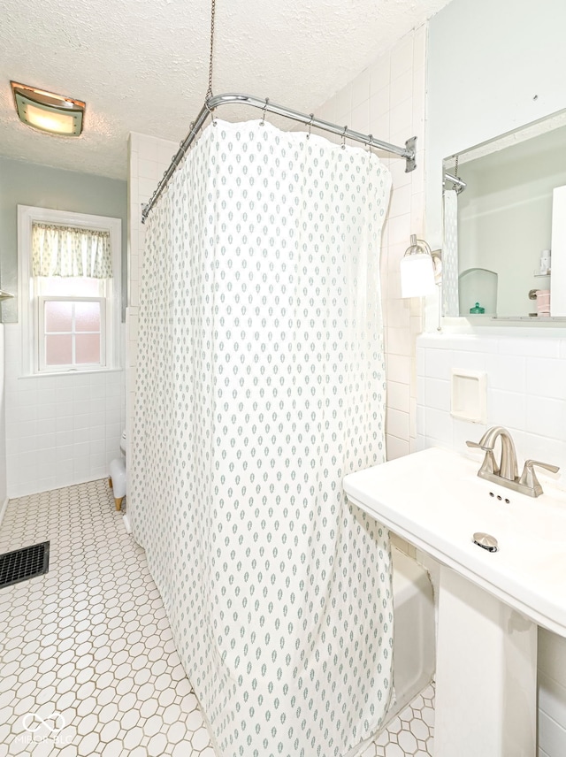 bathroom with tile walls, a shower with curtain, a textured ceiling, and visible vents