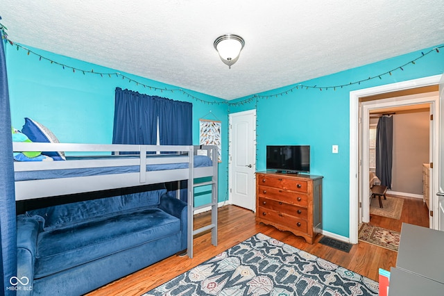bedroom with baseboards, a textured ceiling, and wood finished floors