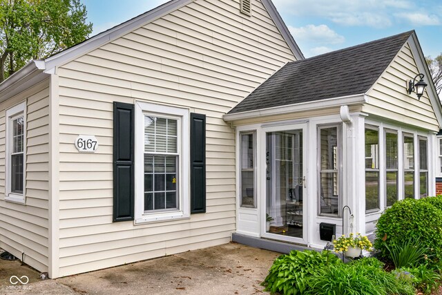 view of home's exterior with a sunroom, a patio, and roof with shingles