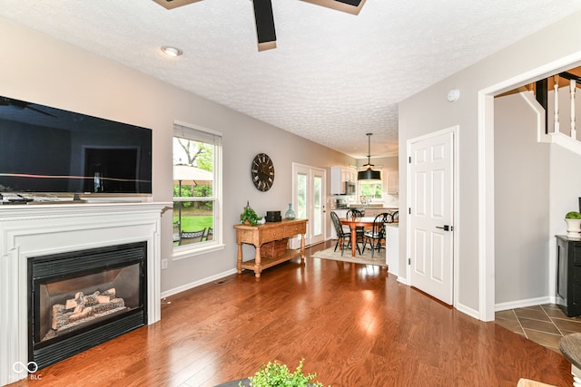 living area with ceiling fan, a textured ceiling, wood finished floors, baseboards, and a glass covered fireplace
