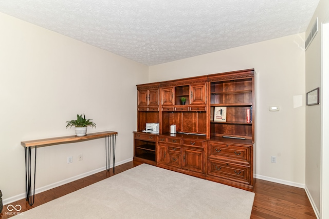 interior space featuring baseboards, a textured ceiling, dark wood-style floors, and visible vents