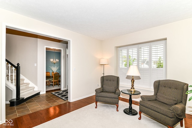 living area featuring a textured ceiling, wood finished floors, stairway, baseboards, and a notable chandelier