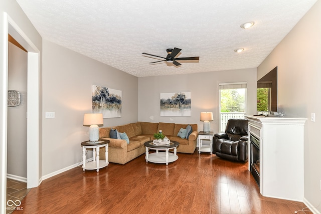living area featuring a ceiling fan, a textured ceiling, baseboards, and dark wood-type flooring