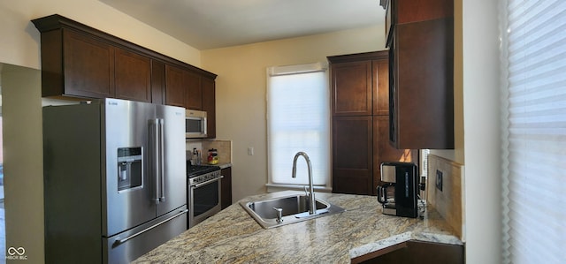 kitchen featuring light stone countertops, dark brown cabinets, a sink, a peninsula, and stainless steel appliances
