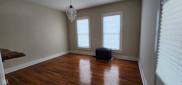 spare room with an inviting chandelier, baseboards, and dark wood-style floors