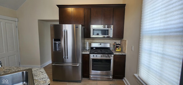 kitchen featuring light stone countertops, dark brown cabinets, tasteful backsplash, a sink, and stainless steel appliances