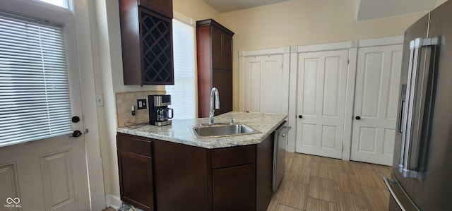 kitchen with dark brown cabinets, light stone countertops, a sink, stainless steel appliances, and a peninsula