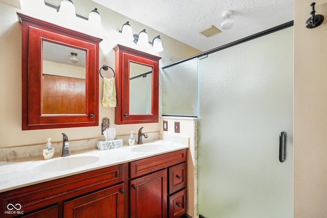 full bath featuring a sink, double vanity, a stall shower, and a textured ceiling