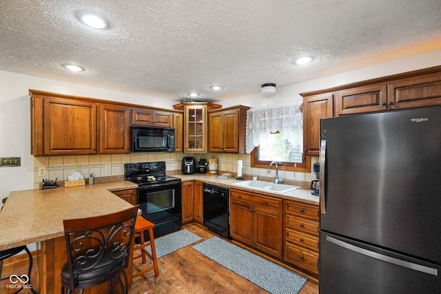 kitchen with a sink, a breakfast bar area, brown cabinetry, a peninsula, and black appliances