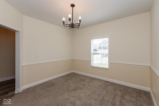 carpeted empty room featuring a chandelier and baseboards