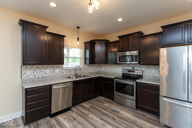 kitchen featuring stainless steel appliances, a sink, dark brown cabinetry, light wood-style floors, and decorative backsplash
