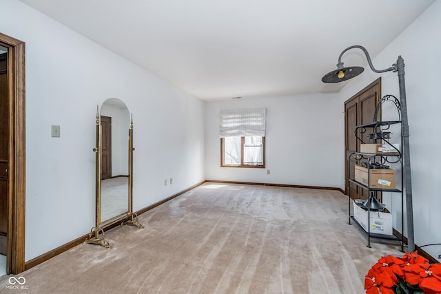 empty room with baseboards, arched walkways, and light carpet