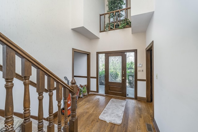 entrance foyer with a high ceiling, baseboards, wood finished floors, visible vents, and stairway