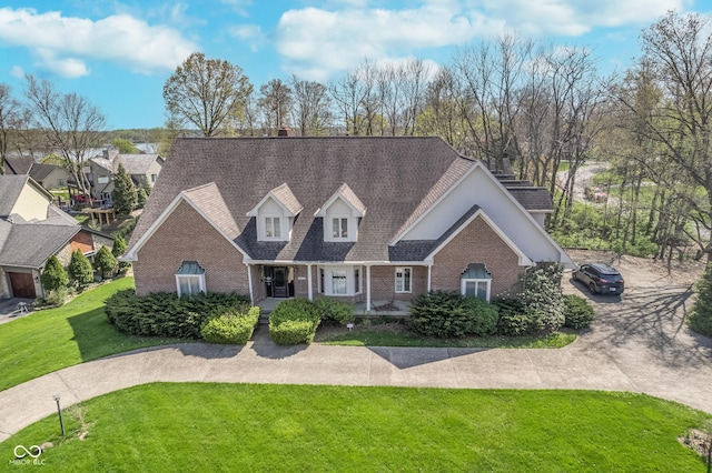cape cod home with brick siding, roof with shingles, a chimney, and a front yard