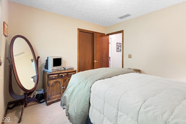 bedroom featuring a textured ceiling, light colored carpet, visible vents, and a closet