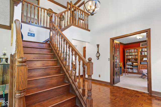 staircase featuring baseboards, ornamental molding, a notable chandelier, and a high ceiling