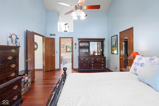 bedroom featuring a ceiling fan, wood finished floors, ensuite bathroom, a towering ceiling, and visible vents