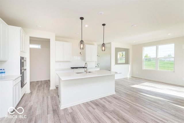 kitchen featuring an island with sink, a sink, a healthy amount of sunlight, light wood-type flooring, and light countertops