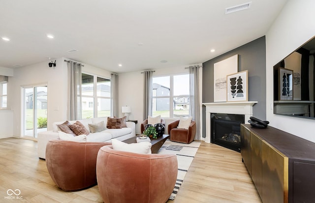 living area featuring a glass covered fireplace, recessed lighting, light wood-style flooring, and visible vents