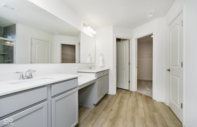 bathroom featuring a sink, two vanities, a shower stall, and wood finished floors