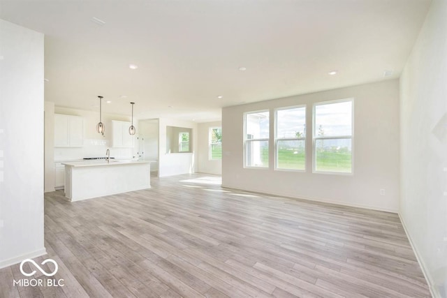 unfurnished living room with light wood-style floors, baseboards, a sink, and recessed lighting