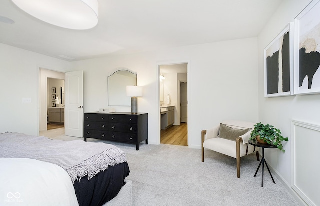 bedroom with baseboards, ensuite bathroom, and light carpet