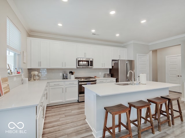 kitchen with ornamental molding, a center island with sink, light wood finished floors, backsplash, and stainless steel appliances