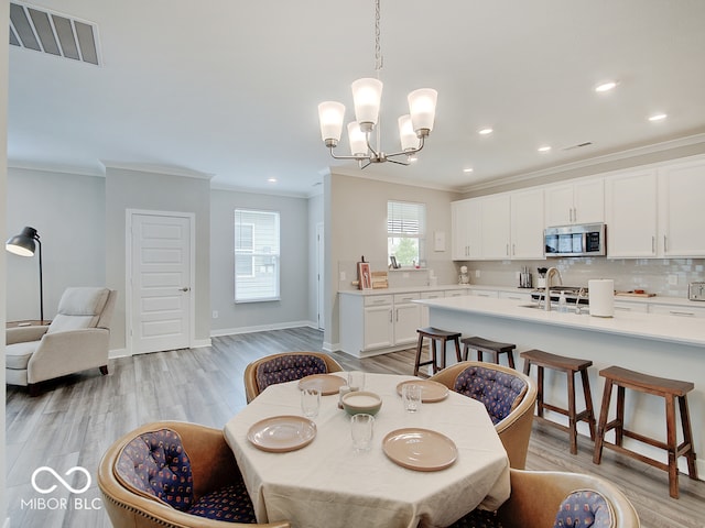 dining room featuring visible vents, ornamental molding, light wood-style floors, and a chandelier