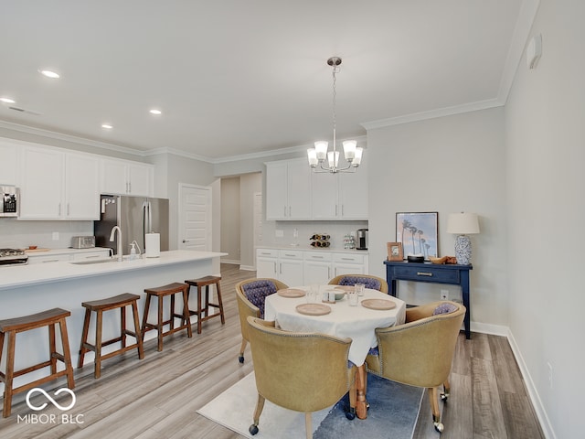dining area with crown molding, baseboards, light wood finished floors, and a chandelier