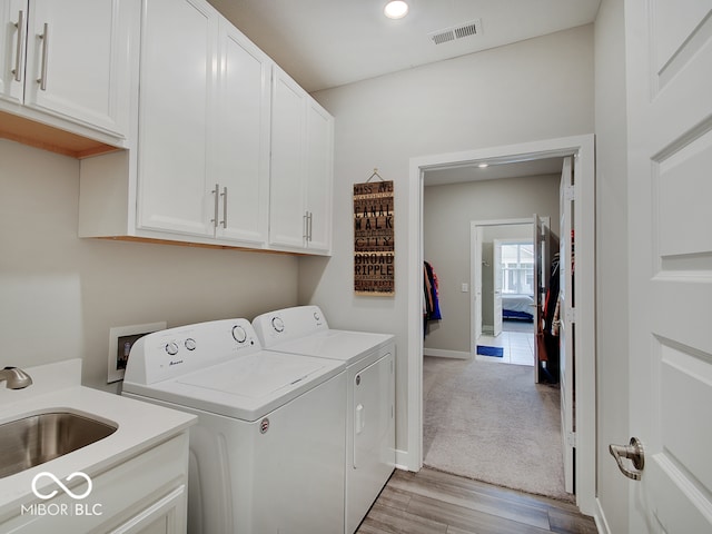 clothes washing area featuring visible vents, washing machine and dryer, light wood-type flooring, a sink, and cabinet space
