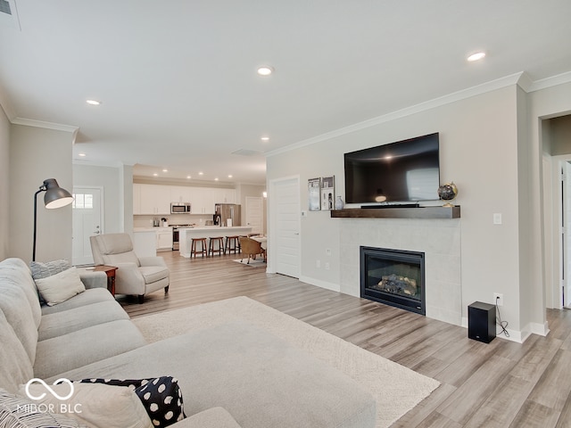 living area with recessed lighting, ornamental molding, light wood finished floors, and a tile fireplace