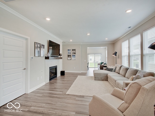 living room with crown molding, visible vents, a glass covered fireplace, recessed lighting, and light wood finished floors