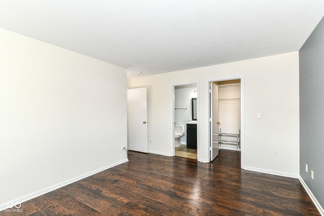 unfurnished bedroom featuring a spacious closet, dark wood-style flooring, baseboards, a closet, and connected bathroom