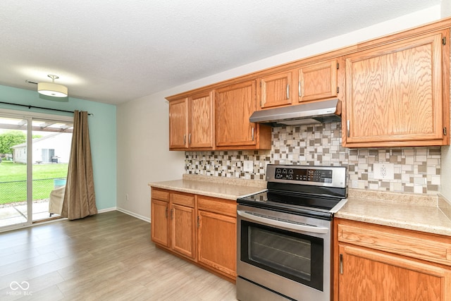 kitchen with stainless steel electric stove, under cabinet range hood, decorative backsplash, light countertops, and a textured ceiling