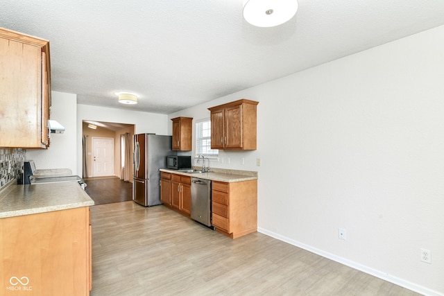 kitchen featuring appliances with stainless steel finishes, light wood-style flooring, light countertops, baseboards, and a sink