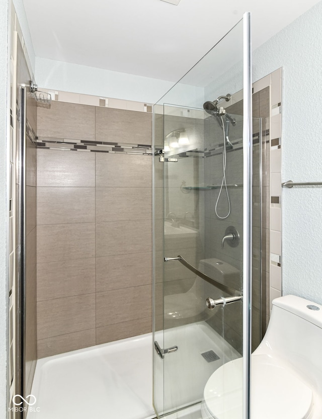 bathroom featuring toilet, a textured wall, and a shower stall