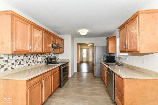 kitchen featuring appliances with stainless steel finishes, under cabinet range hood, decorative backsplash, light countertops, and a sink