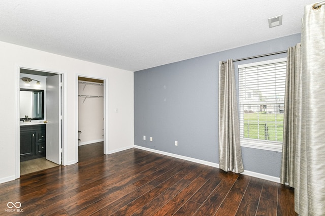 unfurnished bedroom with wood finished floors, baseboards, a spacious closet, a sink, and connected bathroom