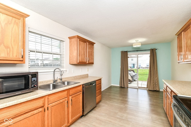 kitchen featuring stainless steel appliances, a sink, light countertops, a textured ceiling, and light wood-type flooring