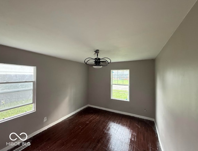 empty room featuring an inviting chandelier, baseboards, and dark wood-style floors