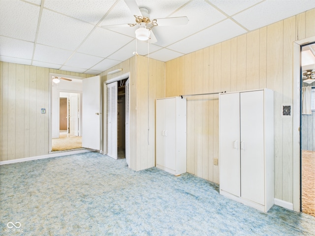 unfurnished bedroom featuring ceiling fan, wood walls, light colored carpet, and a paneled ceiling