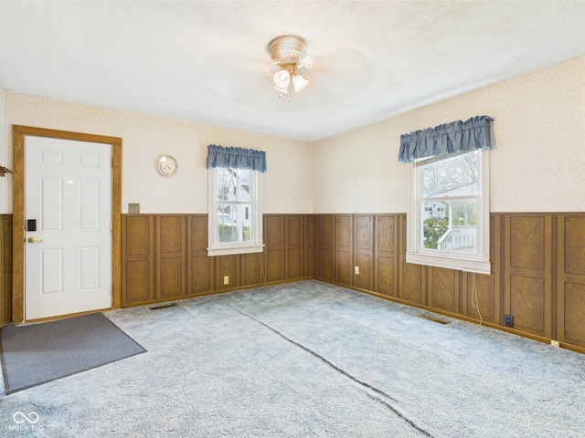 interior space featuring carpet floors, a ceiling fan, wainscoting, and wallpapered walls