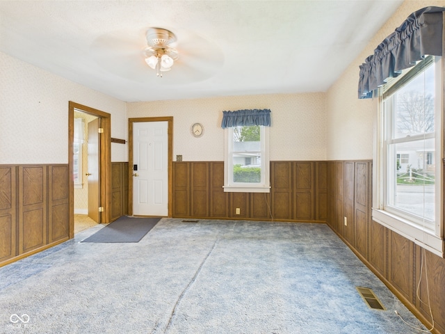 empty room featuring ceiling fan, visible vents, wainscoting, and light carpet